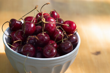 A bowl of ripe cherries is on a wooden table. High quality photo