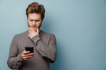 White ginger man with beard frowning and using mobile phone
