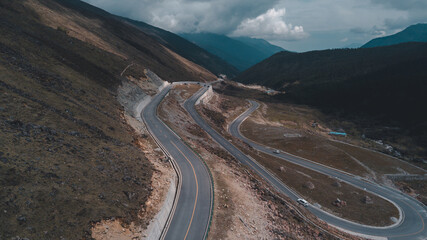 Curved serpentine asphalt road near Kangding on way to Gongga ice mountain in Sichuan, China. Beautiful landscape in fall, early spring. Aerial drone view, peaks and woods. Few vehicles passing by.