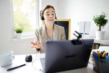 Young woman is learning language with laptop computer, camcorder and headphone online at home....