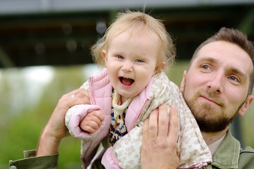 Obraz premium Cute toddler girl having fun on outdoor playground. Young father playing with her little daughter. Spring/summer/autumn active leisure for family with kids.
