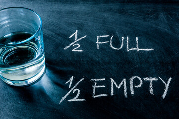 Half-full or half-empty glass of water, with text written on a blackboard, showing optimism or...