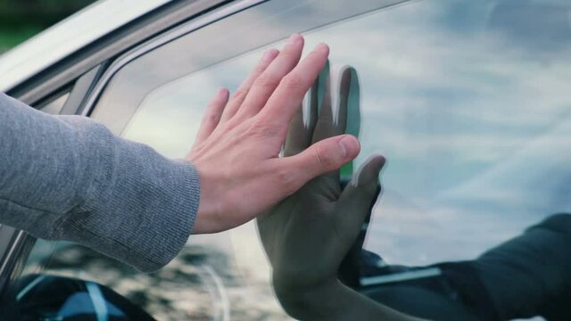Farewell of two people. They put their hands to the glass of the car and then the car drives away