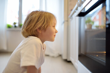 Glad boy sitting on the floor near kitchen stove and waiting for a pie or other baked goods to be prepared. Children love food prepared by their mother. Domestic cuisine