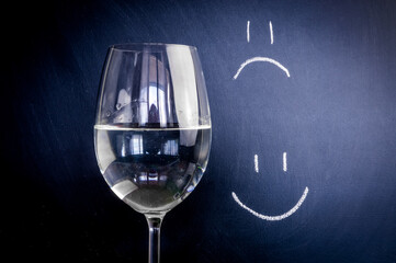 Half-full or half-empty glass of water, with an happy face and unhappy face, showing optimism or pessimism, concept	