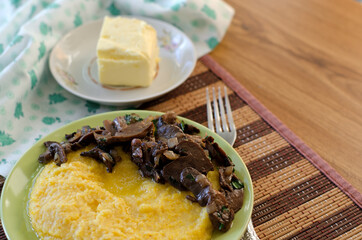 Corn porridge, fried mushrooms with onions and butter in plates on the table.