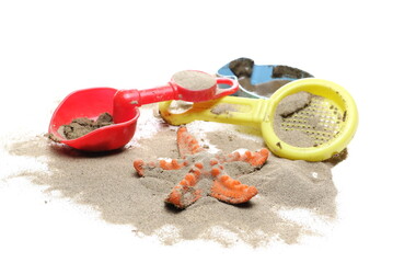 Plastic beach toys and starfish in sand pile isolated on white background