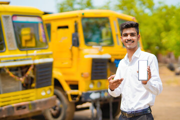 Young indian businessman with his freight forward lorry or truck and showing smartphone.