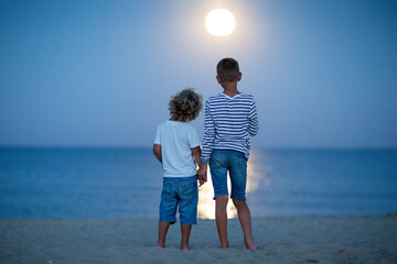 two boys look at the moon by the sea