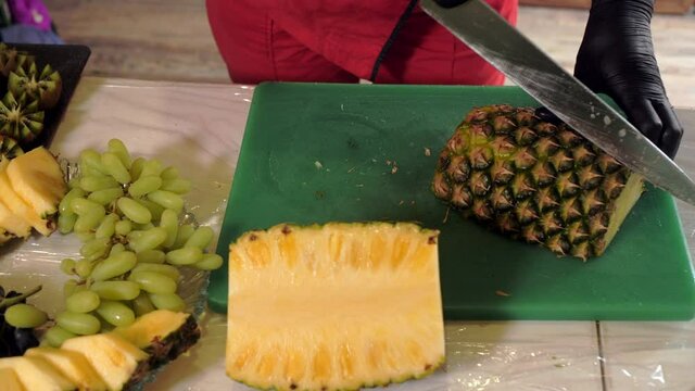 Female shef cutting fresh pineapple for serving fruit snacks. Female hands cutting with knife ripe pineapple.