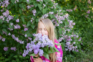 Fototapeta premium Cute blonde girl enjoys the scent of lilacs. City walk. Spring and summer
