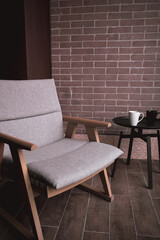 Nice stylish wooden armchair  with brown beige soft pillows on balcony outside near loft welded metal tea table. Couple mugs and ashtray on. Minimalistic interior, place for relaxation and meditation