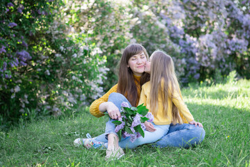 Fototapeta premium Mom and daughter laughing and hugging sitting on a blanket in the park in a clearing. The concept of a happy family, friendship, and love. Outdoor activities