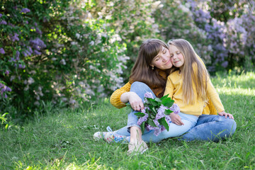 Fototapeta premium Mom and daughter laughing and hugging sitting on a blanket in the park in a clearing. The concept of a happy family, friendship, and love. Outdoor activities