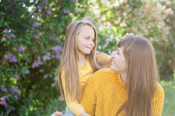Fototapeta premium Mom and daughter laughing and hugging sitting on a blanket in the park in a clearing. The concept of a happy family, friendship, and love. Outdoor activities