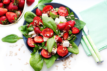 Salad with strawberries, cherry tomatoes, sunflower seeds, spinach and feta cheese on white...