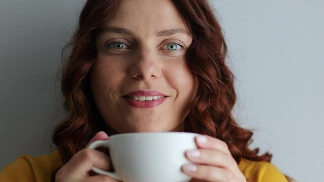 Happy and positive woman enjoying coffee at home during lunch break. Girl inhales the fragrance