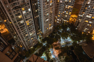 Long exposure night aerial view on residential buildings complex compound. Tall skyscrapers thousands of apartments light illuminates from windows. Small square park inside community. City development