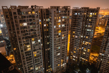 Fototapeta na wymiar Long exposure night aerial view on residential buildings complex compound. Tall skyscrapers thousands of apartments light illuminates from windows. Small square park inside community. City development