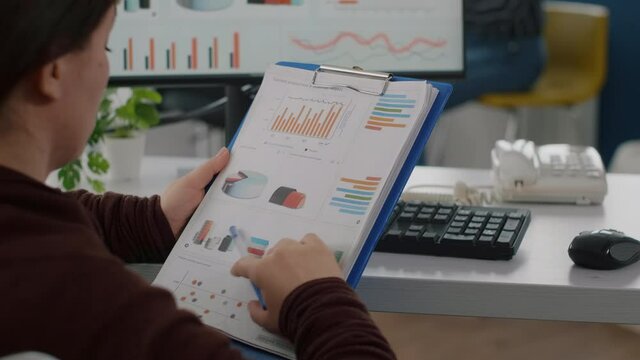 Close up of invalid disabled company director reading project documents holding clipboard checking statistics on computer with data prosessing showing on display. sitting in start up business office