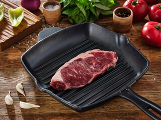 Raw beef steak on grill pan and ingredients around on a wooden table