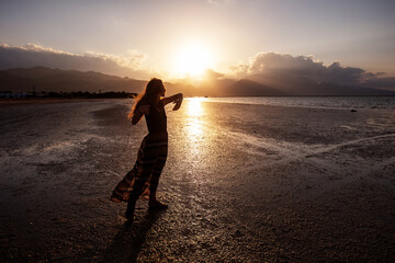 Fototapeta premium Beautiful woman dancing by the sea at sunset