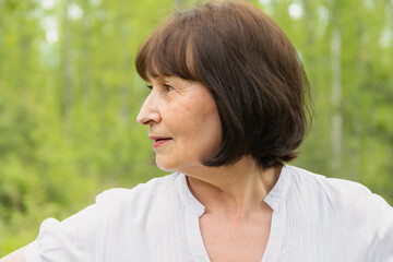Portrait of one woman 60 years old in a summer forest. The woman is depicted in profile