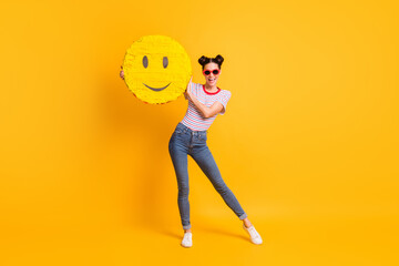 Full length photo of shiny pretty girl dressed striped t-shirt dark glasses holding large smiley pinata isolated yellow color background - obrazy, fototapety, plakaty
