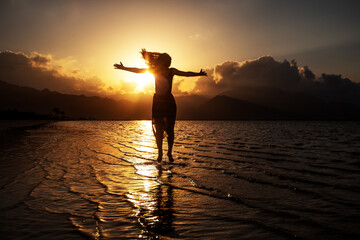 Beautiful woman dancing by the sea at sunset
