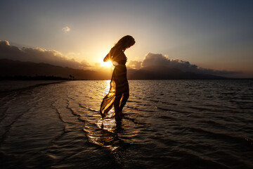 Beautiful woman dancing by the sea at sunset