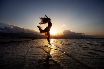 Beautiful woman dancing by the sea at sunset