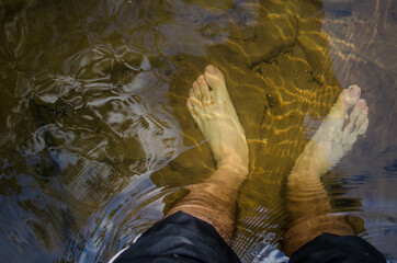 Legs in the water. Crossing the river barefoot.