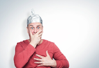 Emotional man in a hat and aluminum foil is scared and grabs his heart with his hand. Fear and...