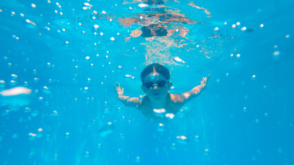 Caucasian Boy with goggles swimming underwater with water sun reflections. Summer vacation holidays...