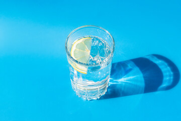 Fresh clean water in a glass with a slice of lemon on a blue background in bright sunlight. Live water, healthy drink