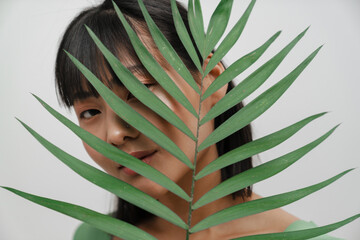 Young asian woman looking at camera while posing with green leaf
