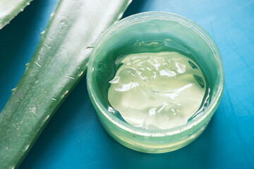 Fresh aloe vera sliced and liquid gel in plastic container on green background 