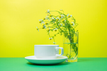A cup of tea on a colored background, next to a small bouquet of field daisies. Delicious soothing tea
