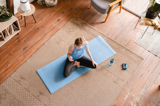 Top view photo of a young fit slim woman training at home for losing weight and fit strong body, shaping exercises on fitness mat, checking sport tracking app during yoga