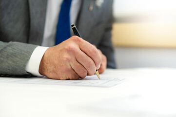 Cropped male holding a pen to sign on a paper. Man wearing suit.