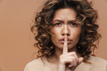 Young hispanic woman frowning while showing silence gesture at camera