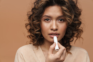 Naklejka premium Young hispanic curly woman applying lipstick and looking at camera