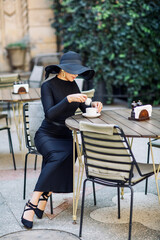 Exquisite woman in a black hat drinks coffee