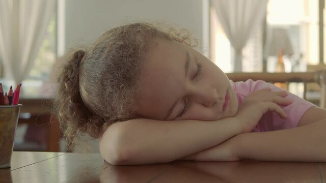 Close-up face of a little girl sleeping baby on her side in her arms. 8 year old girl sleeping sweetly at the table after drawing lesson. 4k footage of a sleeping child who fell asleep after drawing.