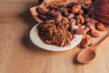 Cocoa powder and cocoa beans with cocoa pods on wooden background.