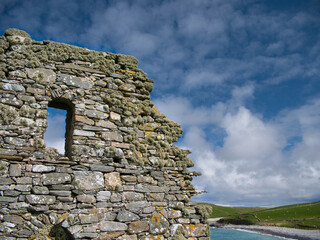 With beard moss lichen, the gable end wall at St Olaf's Church at Lunda Wick, Unst, Shetland, UK - taken on a sunny day with the deserted beach in the background.