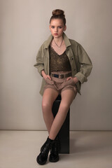 teen girl sitting on a black curbstone in shorts and khaki jackets 