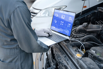 Mechanic using a laptop computer to check collect information during work a car engine. service maintenance of industrial to engine repair.