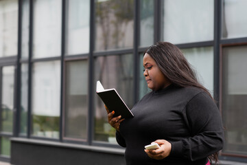 african american plus size woman holding notebook and smartphone outside.