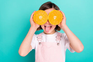 Photo of cute pretty schoolgirl dressed pink overall orange slices cover eyes showing tongue isolated turquoise color background